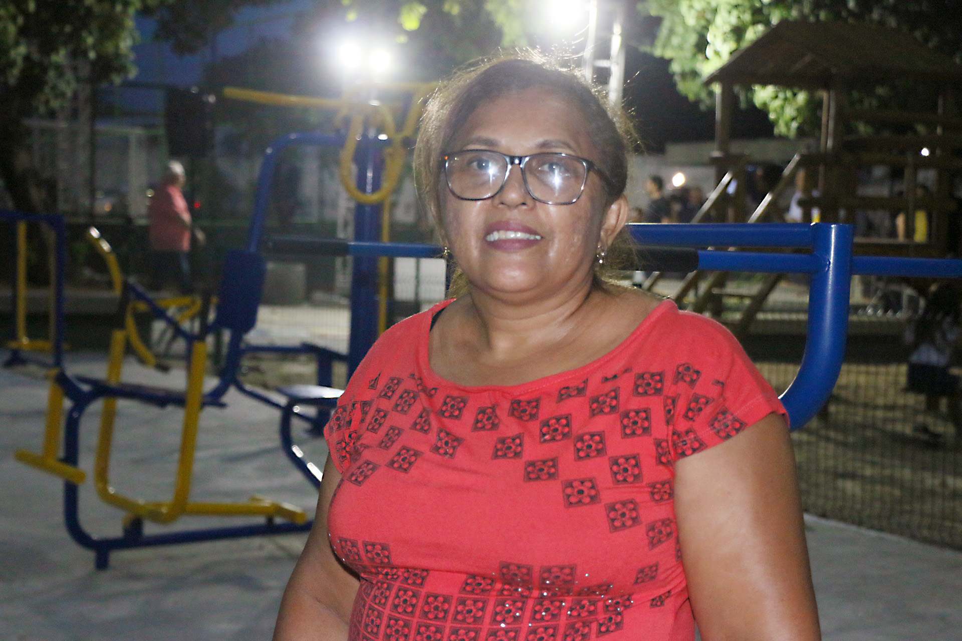 senhora de óculos posando para a foto com academia ao fundo